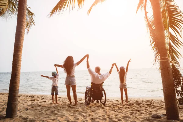 Hombre discapacitado en silla de ruedas con su familia en la playa . — Foto de Stock