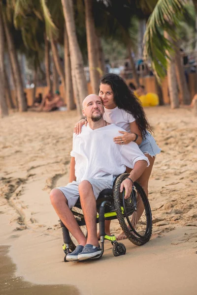 Disabled man in a wheelchair with his wife on the beach. — Stock fotografie