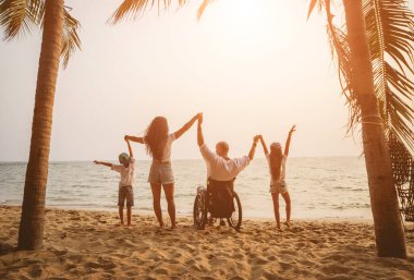 Disabled man in a wheelchair with his family on the beach.