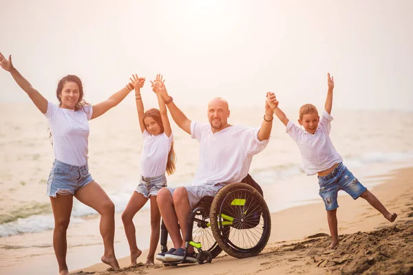 Homem deficiente em uma cadeira de rodas com sua família na praia . — Fotografia de Stock