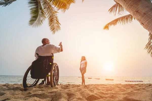 Disabled man in a wheelchair with his wife on the beach. — ストック写真