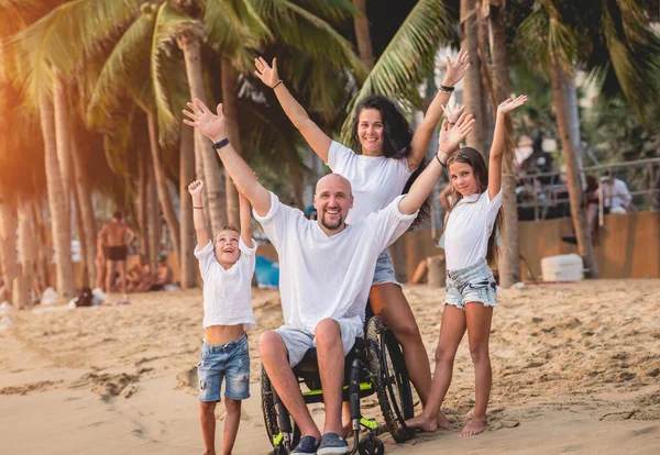 Homem deficiente em uma cadeira de rodas com sua família na praia . — Fotografia de Stock