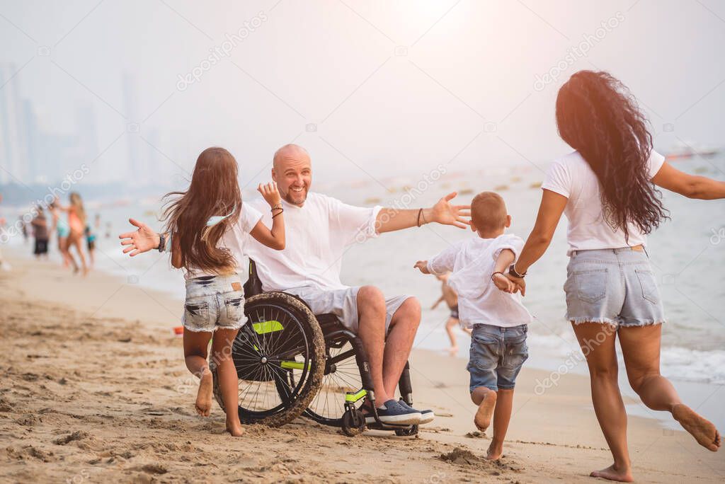 Disabled man in a wheelchair with his family on the beach.
