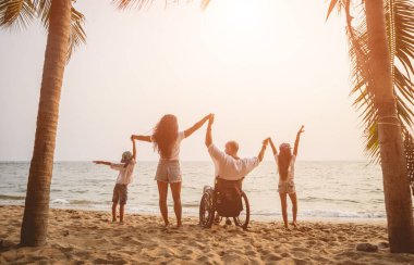Disabled man in a wheelchair with his family on the beach.