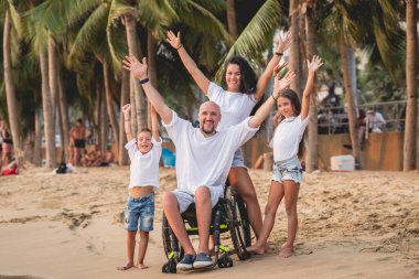 Disabled man in a wheelchair with his family on the beach.