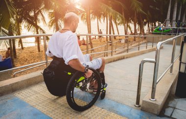 Disabled man in a wheelchair moves on a ramp to the beach.