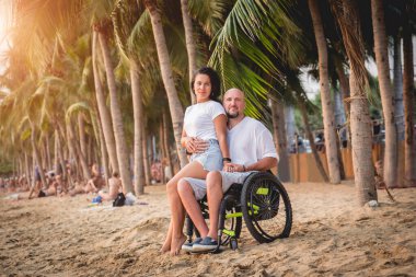 Disabled man in a wheelchair with his wife on the beach.