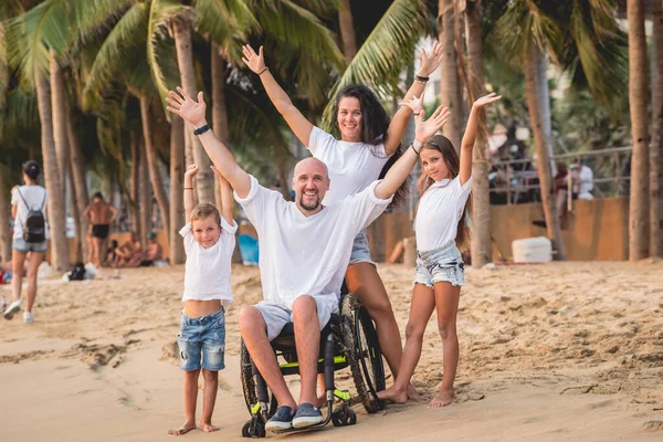 Homem deficiente em uma cadeira de rodas com sua família na praia . — Fotografia de Stock