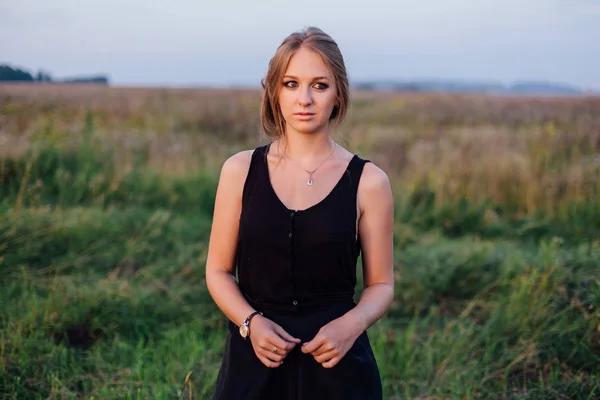 Chica delgada en vestido negro en el campo al atardecer — Foto de Stock