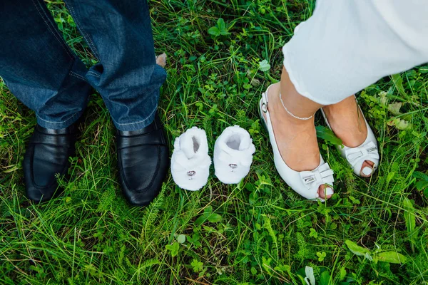 Par de sapatos pequenos entre os pés futuros pais — Fotografia de Stock