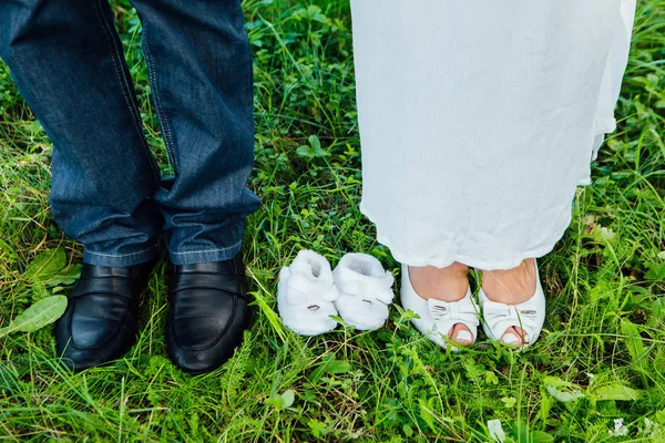 Par de sapatos pequenos entre os pés futuros pais — Fotografia de Stock