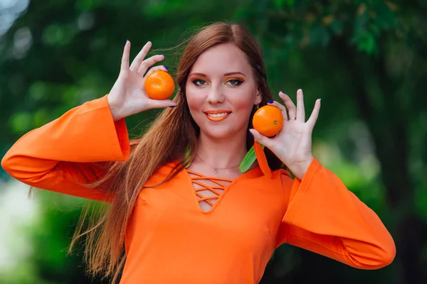 Portrét ženy dost zrzavé vlasy s šťavnaté chutné mandarinky v létě zelený park. — Stock fotografie