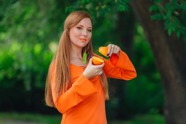 Retrato de mulher de cabelo ruivo bonita com duas metades de suculentas laranjas deliciosas no parque verde de verão . — Fotografia de Stock