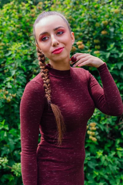 Beautiful young woman with long braid and natural cherry earrings. — Stock Photo, Image