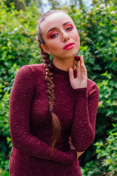 夏の公園でタイトなドレスと天然桜イヤリングを着て長い三つ編みと美しい若い女性 — ストック写真