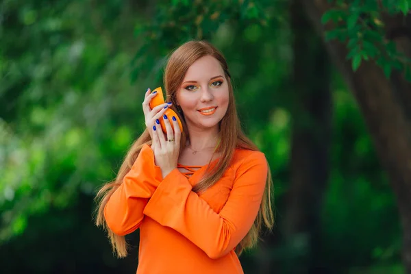 Porträt einer hübschen Frau mit rotem Haar mit zwei Hälften saftig köstlicher Orangen im sommergrünen Park. — Stockfoto