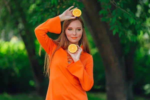 Portrait of pretty red hair woman with two halves of juicy delicious oranges at summer green park. — Stock Photo, Image