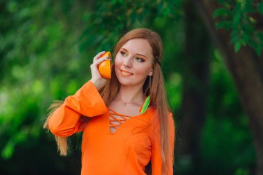 Yaz yeşil Parkı'nda tamamlayan bir sulu lezzetli portakal tutan güzel kızıl saçlı kadın portresi.