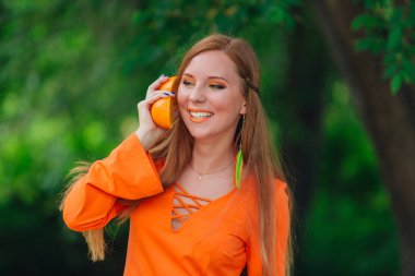 Yaz yeşil Parkı'nda tamamlayan bir sulu lezzetli portakal tutan güzel kızıl saçlı kadın portresi.