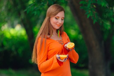 Yaz yeşil Parkı'nda tamamlayan bir sulu lezzetli portakal tutan güzel kızıl saçlı kadın portresi.