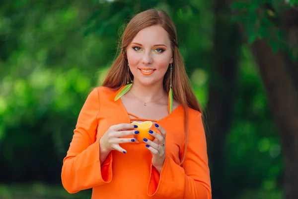 Portrait of pretty red hair woman with juicy delicious orange at summer green park. — Stock Photo, Image