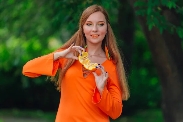 Porträt einer hübschen Frau mit rotem Haar und saftigen Orangen im sommergrünen Park. — Stockfoto