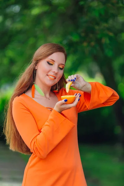 Portrait of pretty red hair woman with juicy delicious orange at summer green park. — Stock Photo, Image