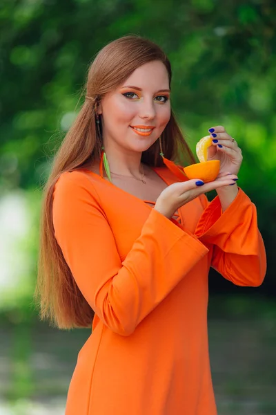 Портрет красивої рудої жінки з соковитим смачним апельсином в літньому зеленому парку . — стокове фото
