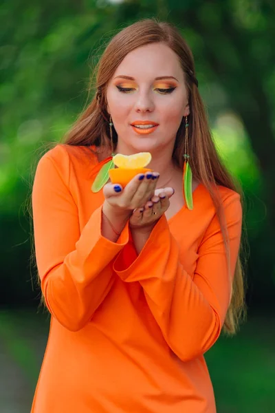 Retrato de bonita mujer pelirroja con jugosa naranja deliciosa en el parque verde de verano . —  Fotos de Stock