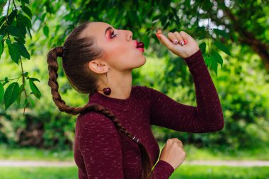 Güzel genç kadın uzun örgü kiraz Küpeli kiraz yaz parkta yiyor..