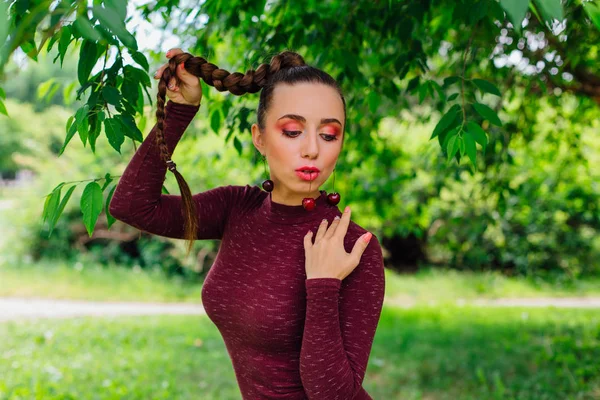 Belle jeune femme avec de longues tresses et des boucles d'oreilles en cerise naturelle . — Photo