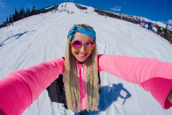 Selfie-Porträt einer jungen, fröhlichen Frau mit Zöpfen auf einer schneebedeckten Piste im Winterskigebiet. — Stockfoto