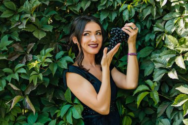 Siyah üzüm ile siyah elbiseli genç seksi esmer portresi. Kopya alanı.