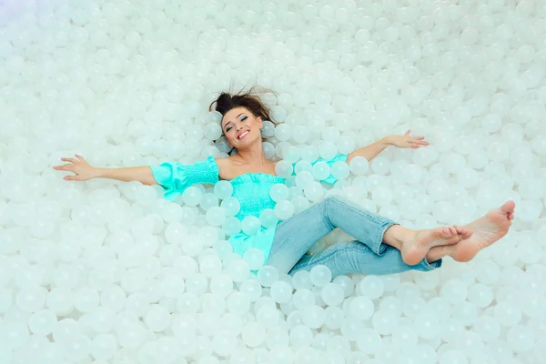 Feliz hermosa mujer yace rodeada de bolas de plástico blanco en la piscina seca para adultos. Copiar espacio . — Foto de Stock