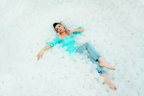 Feliz hermosa mujer yace rodeada de bolas de plástico blanco en la piscina seca para adultos. Copiar espacio . — Foto de Stock