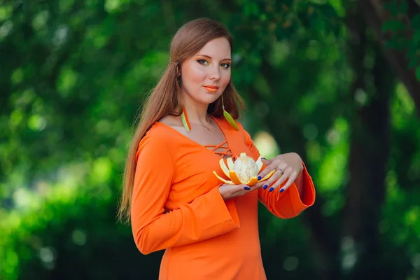 Retrato de bonita mujer pelirroja con jugosa naranja deliciosa en el parque verde de verano . —  Fotos de Stock