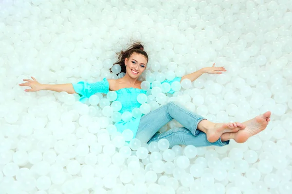 Feliz hermosa mujer yace rodeada de bolas de plástico blanco en la piscina seca para adultos. Copiar espacio . — Foto de Stock