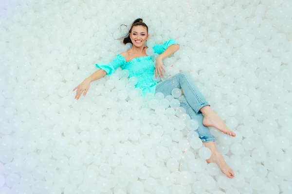 Feliz hermosa mujer yace rodeada de bolas de plástico blanco en la piscina seca para adultos. Copiar espacio . — Foto de Stock