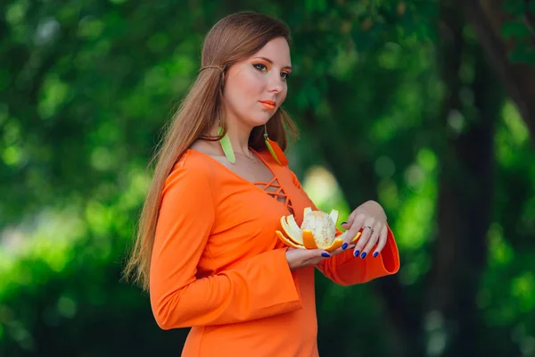 Retrato de bonita mujer pelirroja con jugosa naranja deliciosa en el parque verde de verano . —  Fotos de Stock