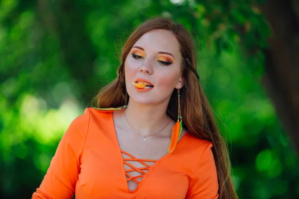 Retrato de bonita mujer pelirroja con jugosa naranja deliciosa en el parque verde de verano . — Foto de Stock