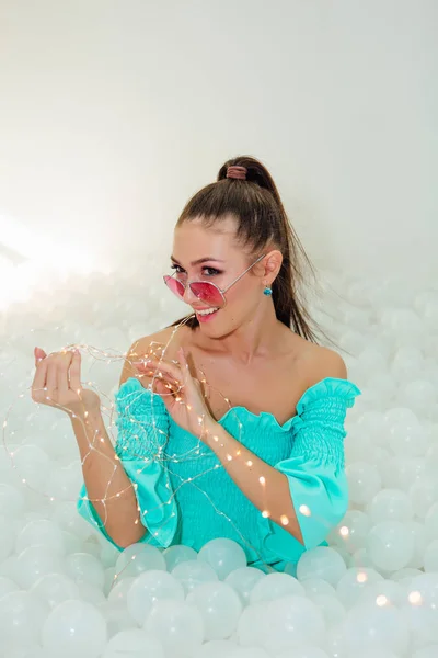 Feliz hermosa mujer yace rodeada de bolas de plástico blanco con guirnalda — Foto de Stock