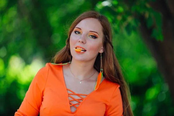 Retrato de bonita mujer pelirroja con jugosa naranja deliciosa en el parque verde de verano . — Foto de Stock