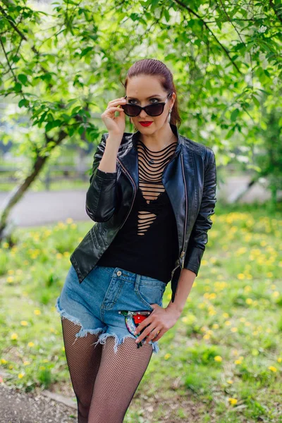 Charming woman dressed in a leather jacket near bird-cherry tree — Stock Photo, Image