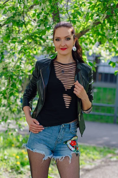 Mujer encantadora vestida con una chaqueta de cuero cerca de árbol de cerezo pájaro — Foto de Stock