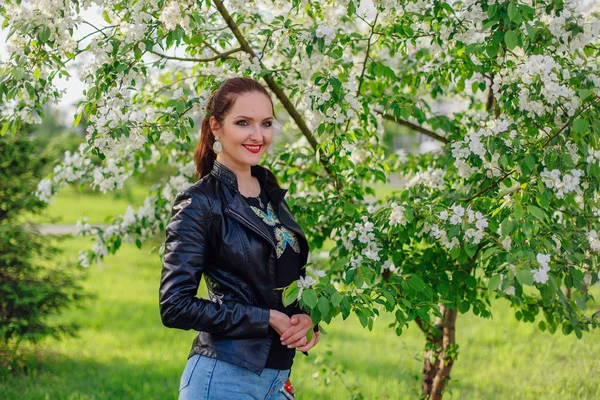 Charmante vrouw gekleed in een lederen jas onder de appelboom — Stockfoto