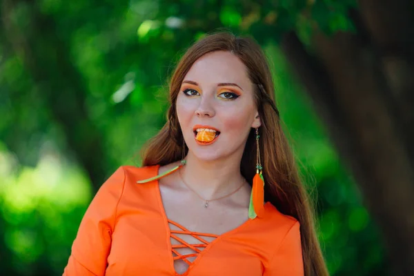 Porträt einer hübschen Frau mit rotem Haar und saftigen Orangen im sommergrünen Park. — Stockfoto