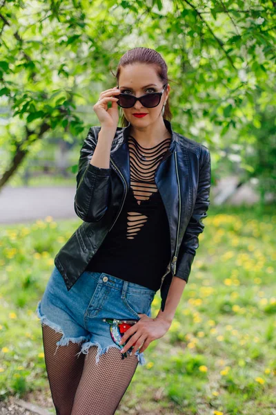 Mujer encantadora vestida con una chaqueta de cuero cerca de árbol de cerezo pájaro — Foto de Stock