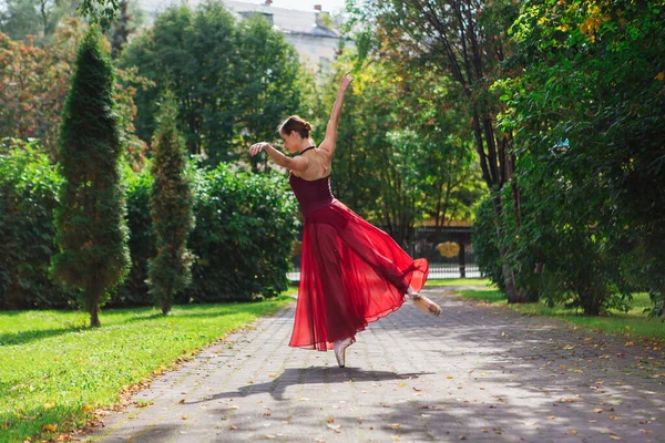 Bailarina de mujer en vestido de ballet rojo bailando en zapatos puntiagudos en el parque de otoño . —  Fotos de Stock