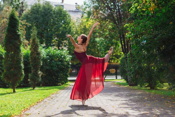 Ballerina donna in abito da balletto rosso che balla in scarpe da punta nel parco autunnale . — Foto Stock