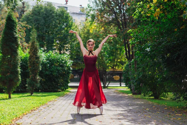 Woman ballerina in red ballet dress dancing in pointe shoes in autumn park.